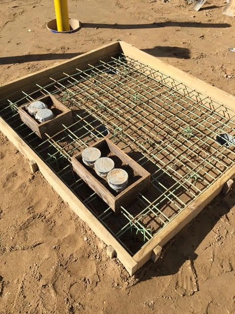 A formed concrete pad with a rebar grid and conduit stub-ups boxed out for an underground feed.