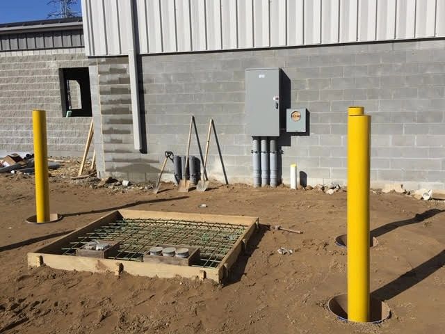 A formed pad with a rebar grid and conduit stub-ups beside a new meter and disconnect on a block wall.
