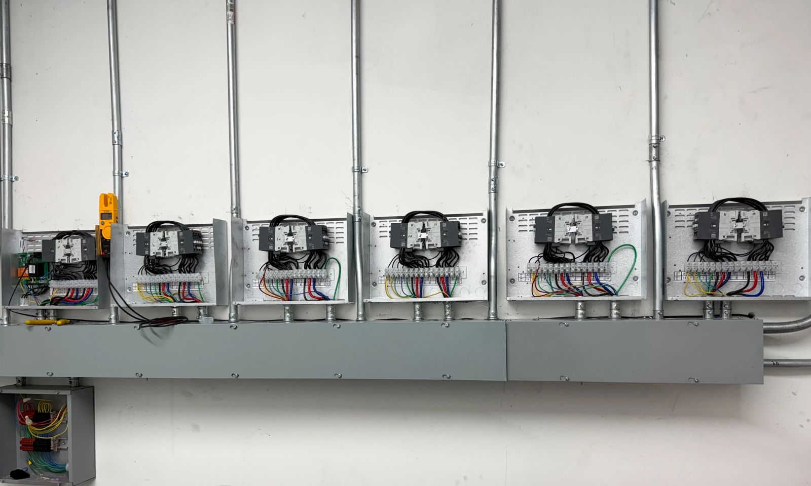A row of six wall-mounted disconnects wired down to a shared wireway, fed by rigid conduit runs.