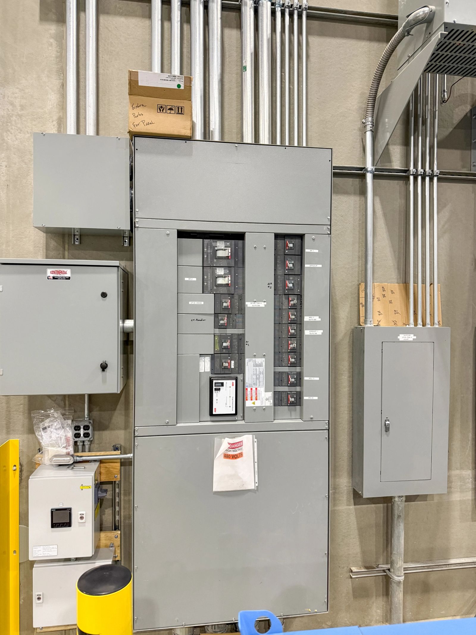 A 480-volt switchboard flanked by panelboards and control cabinets, fed by racked rigid conduit.