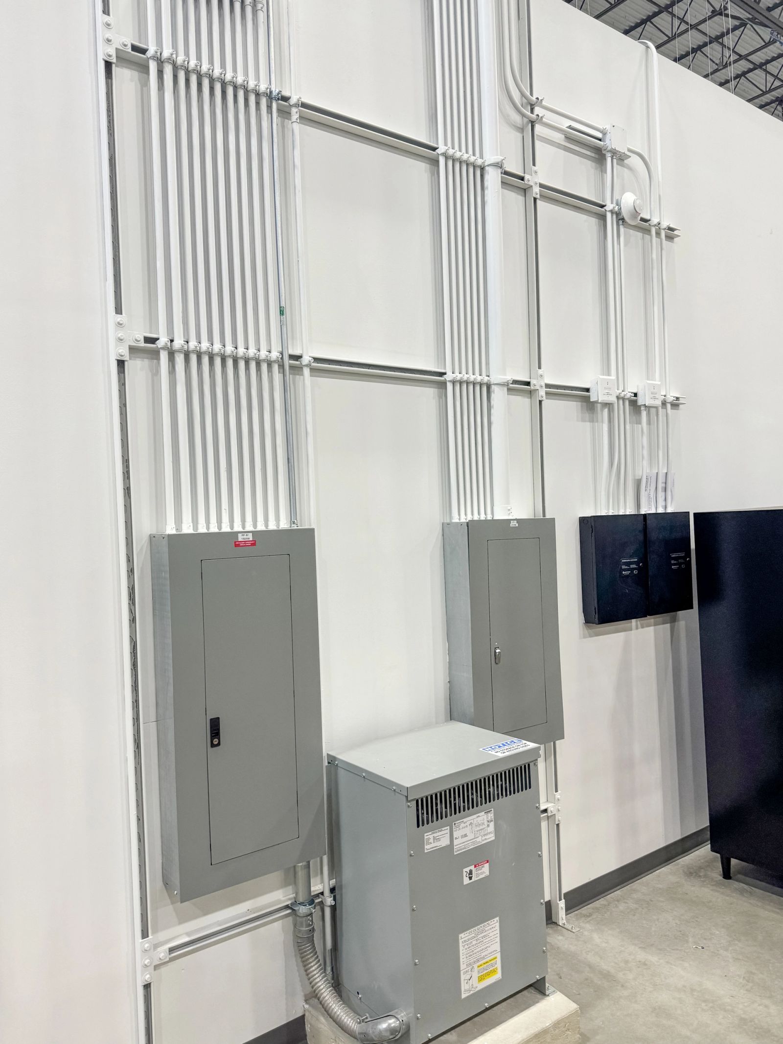 Two commercial panelboards and a floor-mounted dry-type transformer fed by neatly racked conduit.