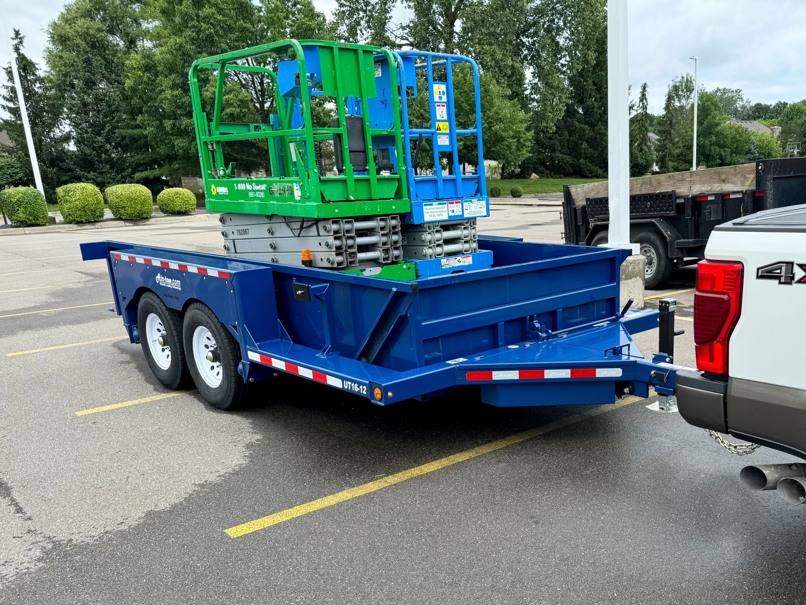 A scissor lift loaded and strapped onto a trailer behind the crew truck, ready for the next job.