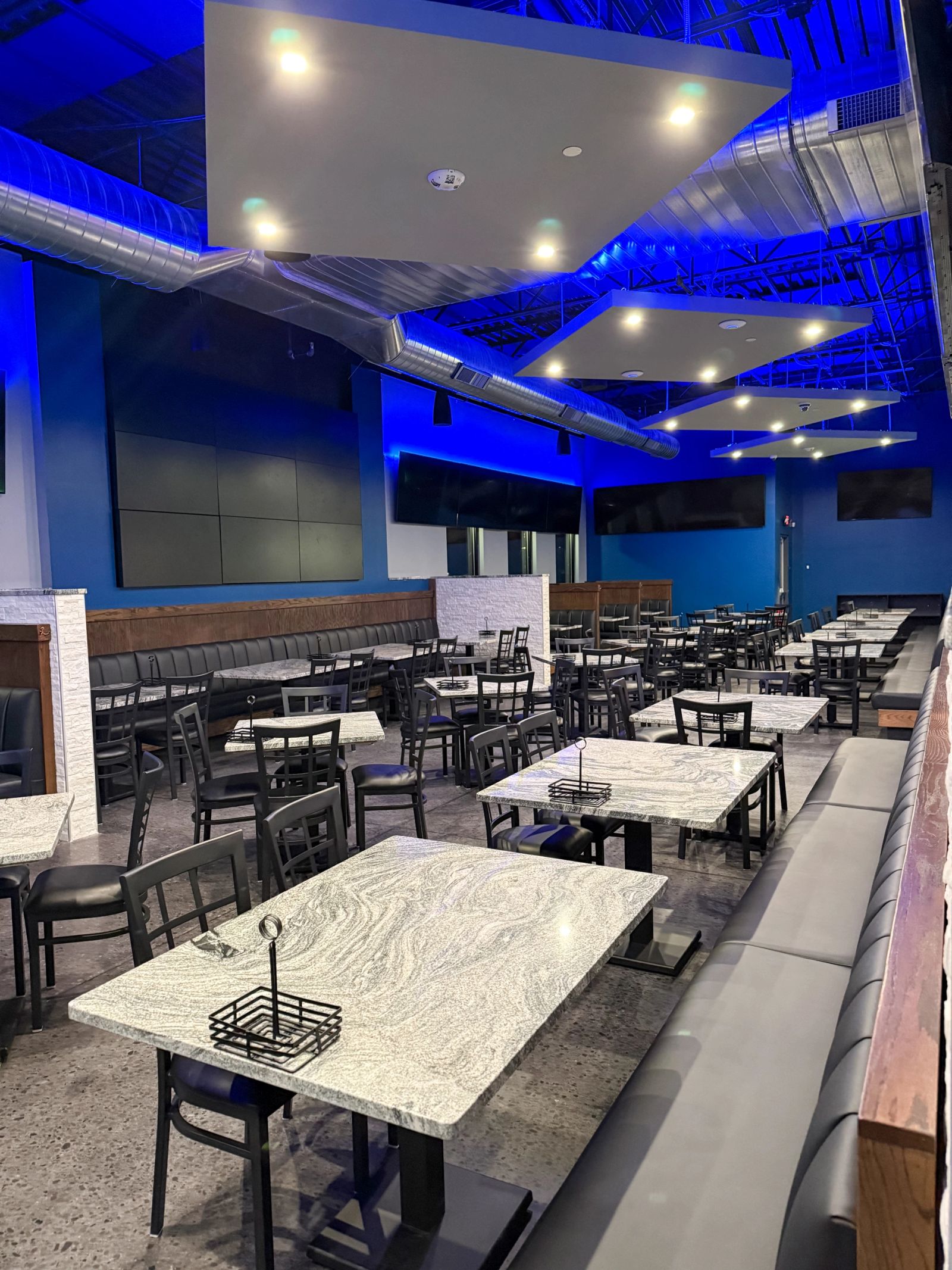 A restaurant dining room lit by recessed cans set into floating ceiling clouds, with blue perimeter cove lighting.