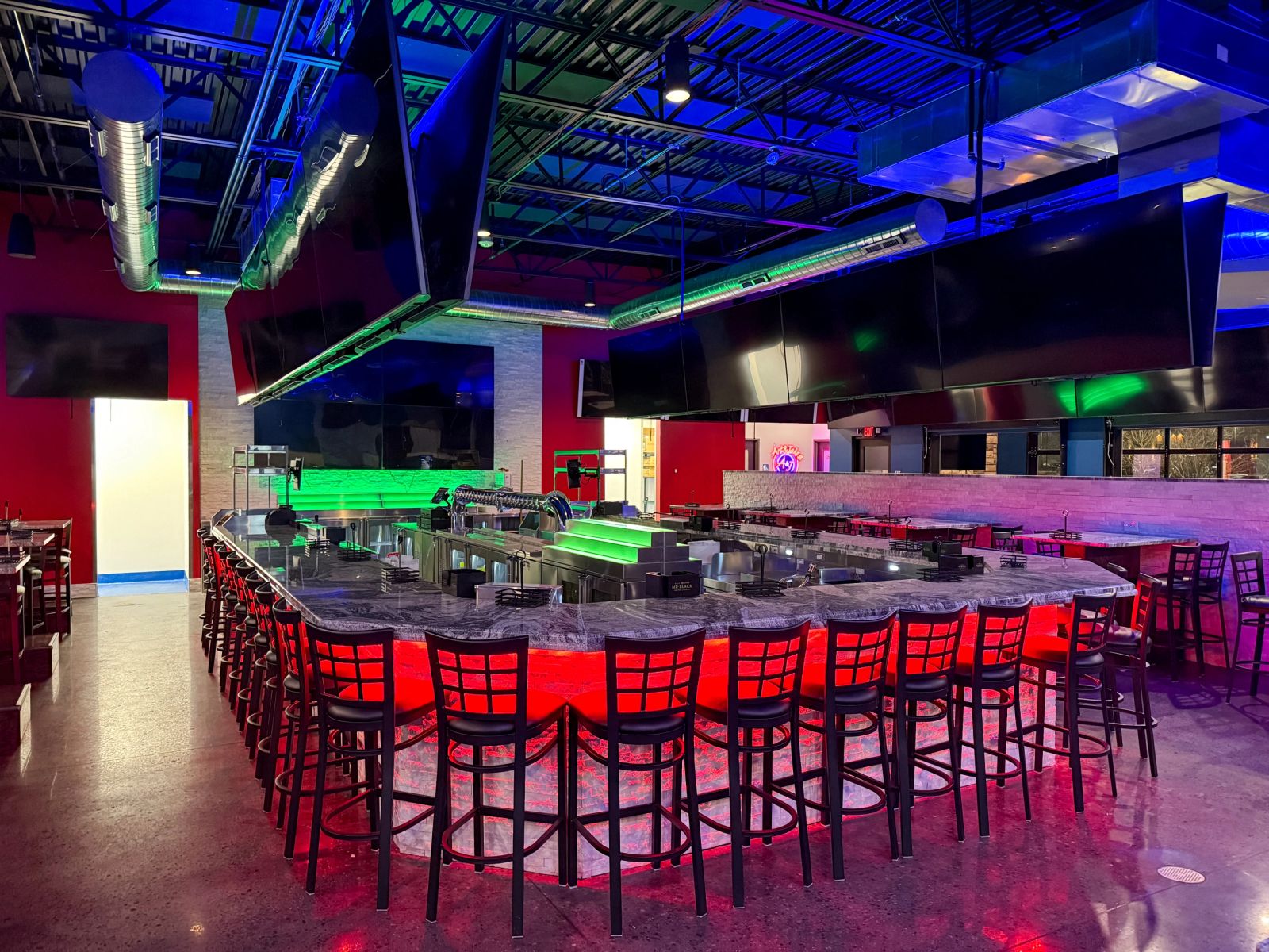 A finished sports bar: colour-changing cove lighting under a granite bar top and a ring of overhead televisions.