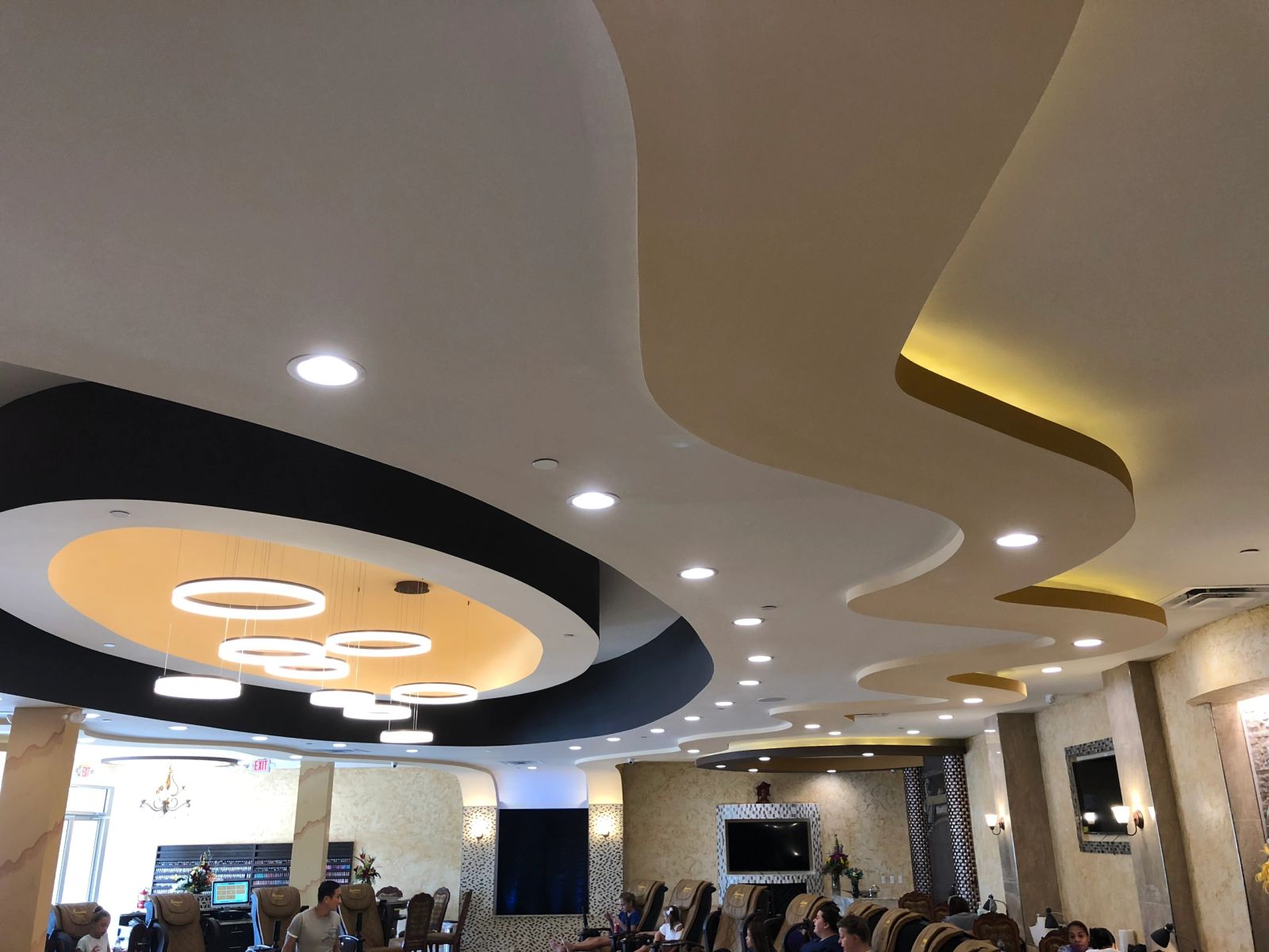 Sculpted curved ceiling with recessed cans, hidden cove lighting and suspended ring pendants.