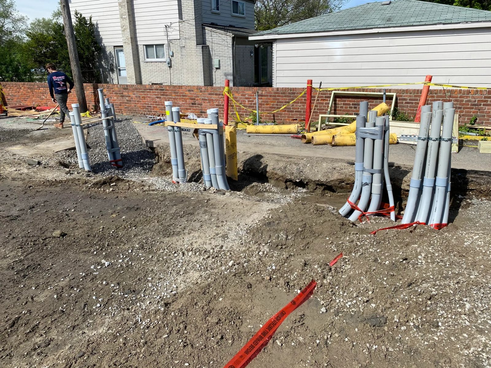 Bundles of grey conduit strapped to stakes and stubbed up out of an open trench on a residential lot.
