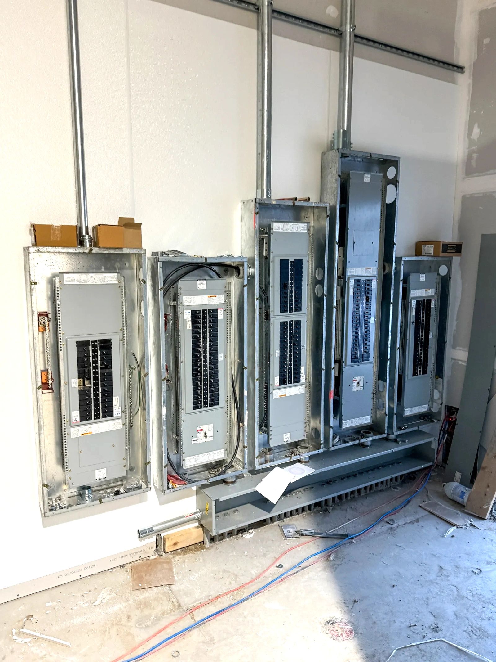 Five panelboard enclosures set on a shared wireway during rough-in, with conduit dropped from above.