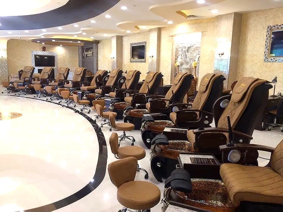 A row of pedicure stations lit by recessed cans under a layered, curved ceiling.
